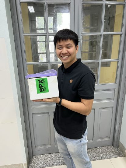 Tan holds a box and smiles.